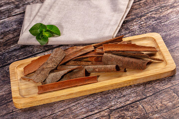 Cinnamon sticks on light wooden tray with fresh mint leaves and linen napkin against rustic dark wood background © Andrei Starostin