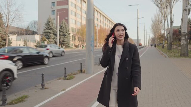 Stylish young woman talking on phone while walking on city street
