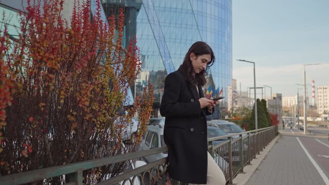 Young woman using smartphone while leaning on fence in city