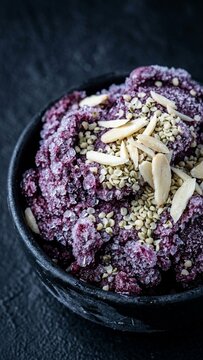 Purple berry sorbet acai bowl topped with sliced almonds and seeds on dark stone background