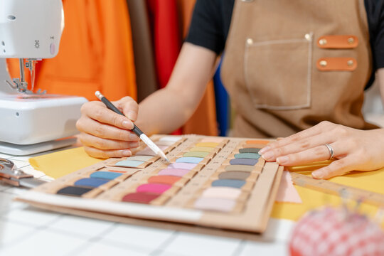 Professional fashion designer selecting fabric colors and sewing accessories in a modern studio. Creative textile design, garment production, tailoring craftsmanship and apparel development.