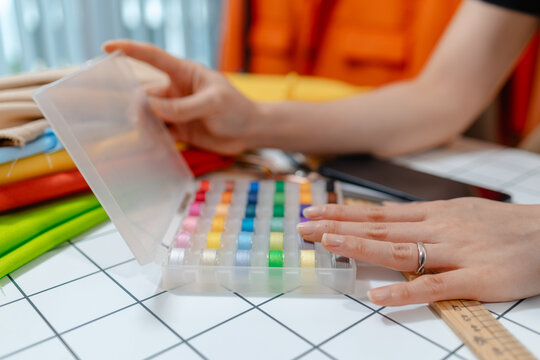 Professional fashion designer using a smartphone while managing a sewing studio and organizing tailoring supplies. Creative apparel production, small business and handmade craftsmanship.
