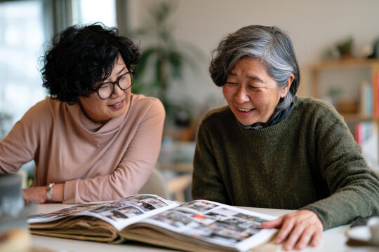 Two older women sit together, reminiscing and sharing a scrapbook filled with memories, highlighting the importance of connection and storytelling across generations.