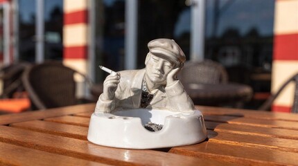 Obraz premium Ceramic ashtray with male figurine holding cigarette on outdoor café table 