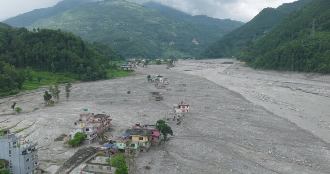 Betrawati Nepal, aerial shot of a row of multi-story residential buildings heavily surrounded and partially buried by an extensive plain of gray mud silt following a glacial outburst