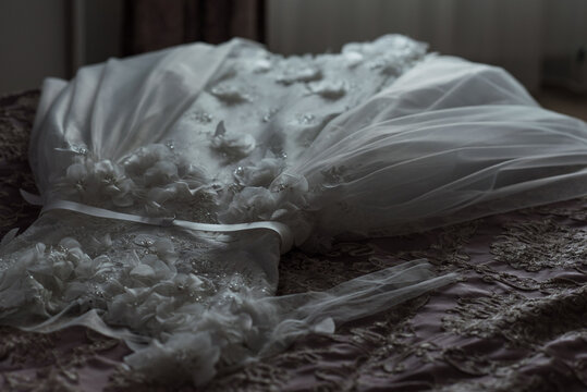 Elegant wedding dress lying on bed during bride preparation.