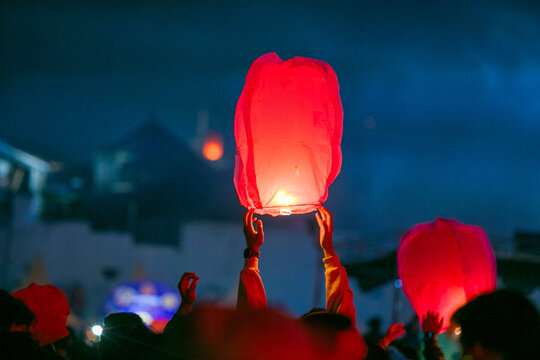 Hands holding a glowing green paper sky lantern ready to release during lantern festival at night with bokeh light background, copy space included.