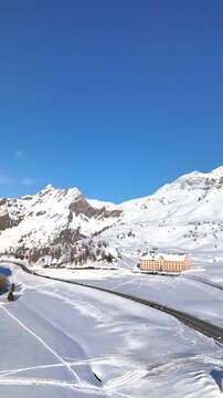 Aerial. Cars drive along scenic snow-covered Simplon Pass with Hospice building