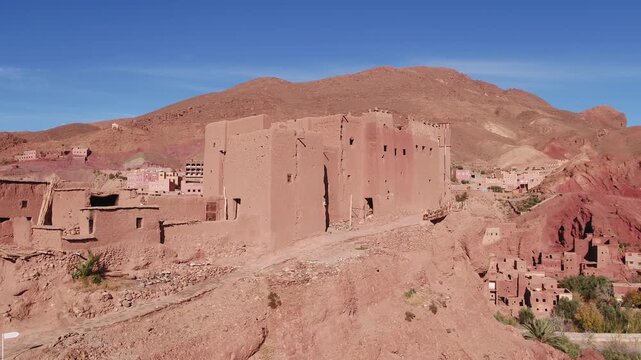 Elevated aerial perspective capturing the massive rammed-earth defensive facade, narrow arrow slits, and fortified structure of an ancient Berber kasbah in Tinghir, Morocco.