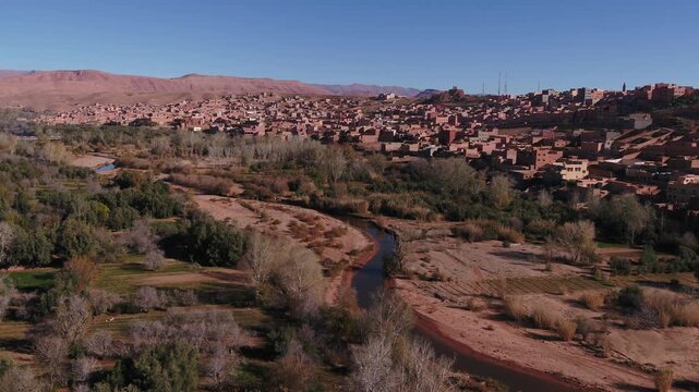 Elevated aerial perspective capturing the dense mudbrick architecture and urban layout of a traditional hillside settlement bordering the Todra valley in Morocco.