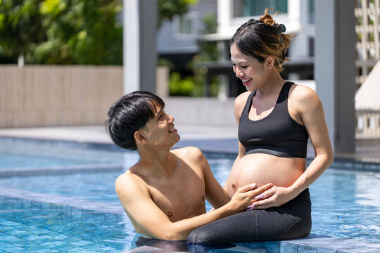 Heavily pregnant asian woman in her third trimester is enjoying her leisure time at the swimming pool with her husband in relax and calm for maternity and happy family and motherhood parenting concept