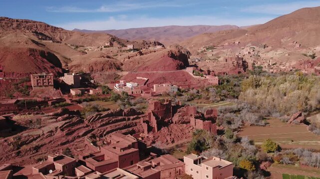 Expansive elevated aerial panorama capturing the layered settlement morphology, traditional clay rooftops, and rugged red canyon hills across the Todra valley in Morocco.