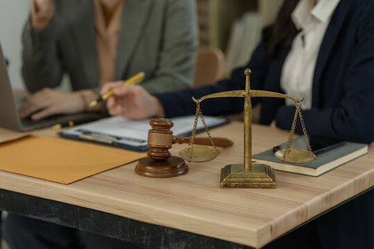 Lawyers discussing legal documents and contract terms with wooden gavel and justice scale on desk in office.