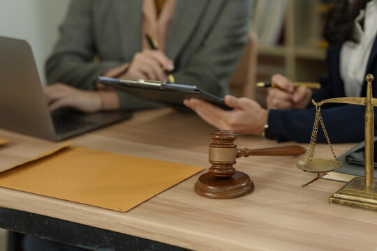Lawyers discussing legal documents and contract terms with wooden gavel and justice scale on desk in office.