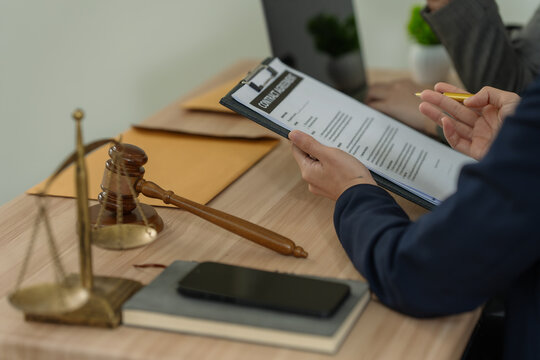 Lawyers discussing legal documents and contract terms with wooden gavel and justice scale on desk in office.