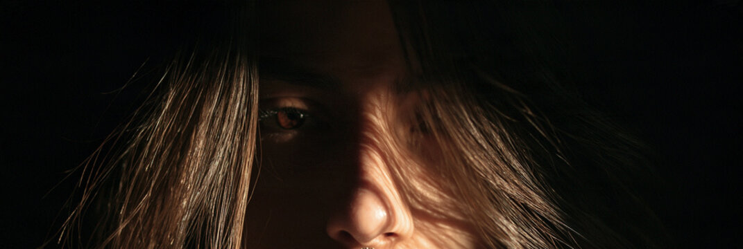 Gesicht mit langen Haaren, halb im Schatten, Lippen und Nase im warmen Licht vor dunkelbraunem Hintergrund, filmischer Stil, f&uuml;r Modekampagnen, Blog-Header oder Plakate.
