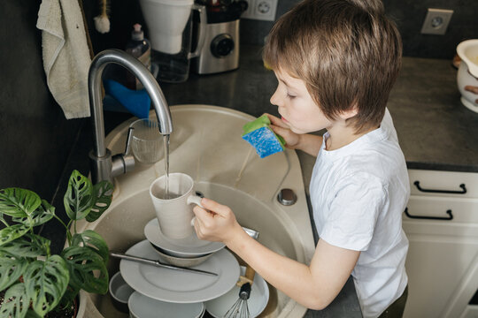 Boy washing dishes in kitchen sink doing chores