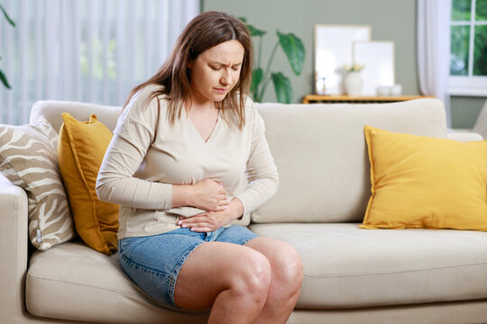 Young woman sitting on the couch at home with a pain in her stomach