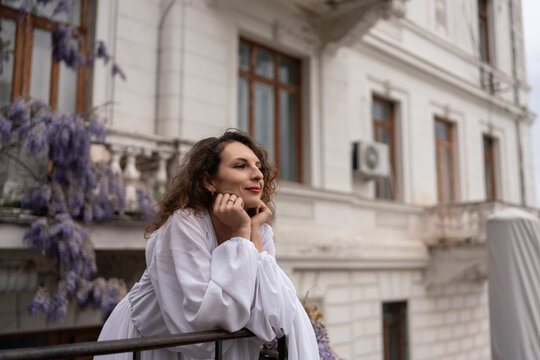 Elegant woman posing gracefully on a balcony outdoors by a historic white building during a sunny day