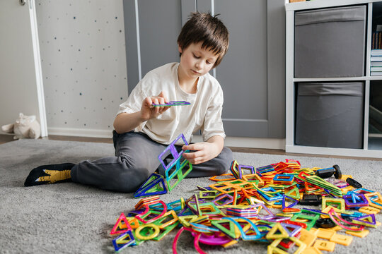 Young boy building magnetic tiles on carpet floor
