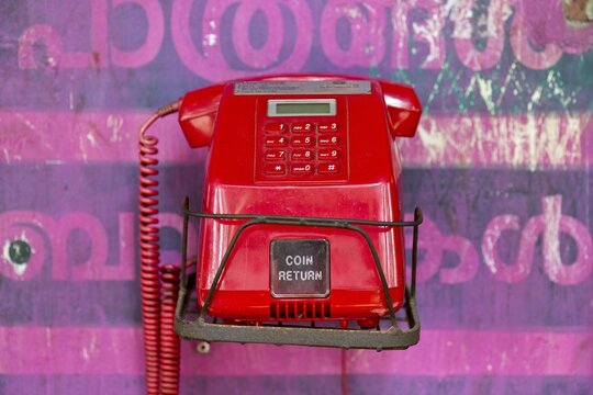Old red telephone against a wall with pink Malayalam script, Kerala, India