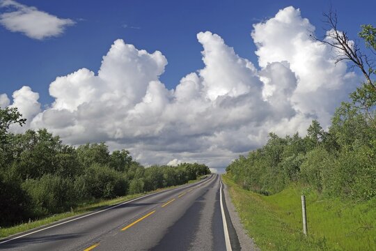 Endless straight road leads up and down through forests, huge clouds (cumulus), deserted wilderness, Utsjoki, Lapland, Finland
