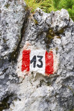 Red and white hiking trail marker sign number 13 painted on textured alpine rock face route navigation signpost Dolomites Alps Italy