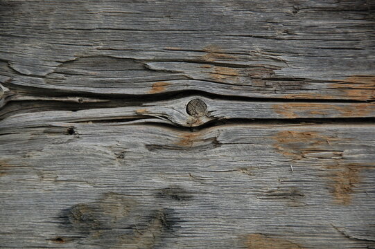 Close-up of aged weathered wooden planks with cracked, peeling, and rough natural grain. Gray and brown tones create a rustic, distressed surface texture suitable for backgrounds, vintage designs, con