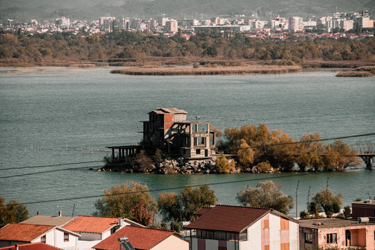A derelict multi-story concrete and brick structure standing on a small islet in the middle of a lake