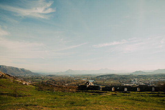 A grassy hillside overlooking a broad river valley with historic ruins and distant mountains