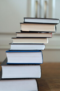 Tall stack of closed hardcover books forms an uneven column on a table. Concept of reading, education, accumulated knowledge, study resources and lifelong learning.