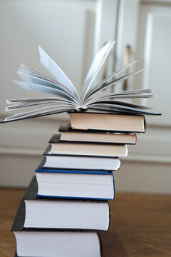 Open book with fanned pages balances on a leaning stack of hardcover books. Concept of reading, education, knowledge growth, intellectual development and lifelong learning.