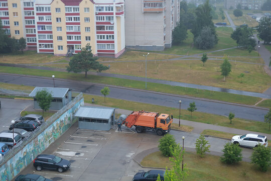 Municipal waste collection truck removes household waste beside a residential apartment building. Concept of garbage collection, sanitation services, waste management and urban cleanliness.