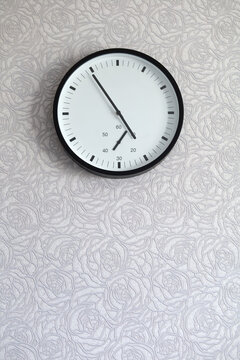 Round analog wall clock hangs high on patterned wallpaper with large copy space below. Concept of time management, deadline, waiting, schedule, punctuality and passing time.
