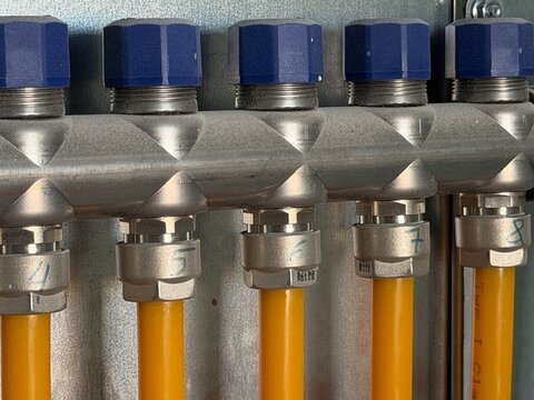 Heating manifold connections distributing warm water through yellow pipes and blue caps, representing efficient underfloor heating system technology for home comfort and energy management