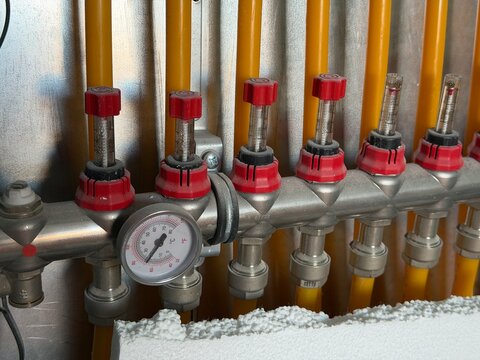 Heating manifold feeding yellow pex underfloor heating circuits with red flow meters, control valves and a thermometer showing water temperature in new residential installation