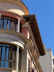 Elegant building facade with large arched windows reflecting blue sky, decorative moldings, detailed cornice and classic roof tiles, showcasing traditional mediterranean design © Tetyana
