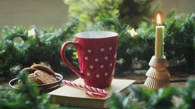 Person enjoying warm cup of tea or coffee with festive Christmas decorations in background. Atmosphere is cozy and perfect for winter.