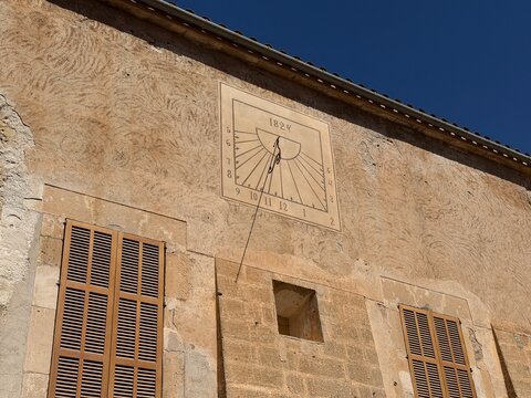 Historic sundial from 1824 marking time on a textured stone building wall with traditional wooden shutters, reflecting ancient timekeeping in manacor, balearic islands, spain