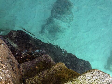Calm turquoise water rippling gently over a rocky shoreline, revealing the textured rocks below and reflecting light, highlighting the clarity and natural beauty of the mediterranean sea