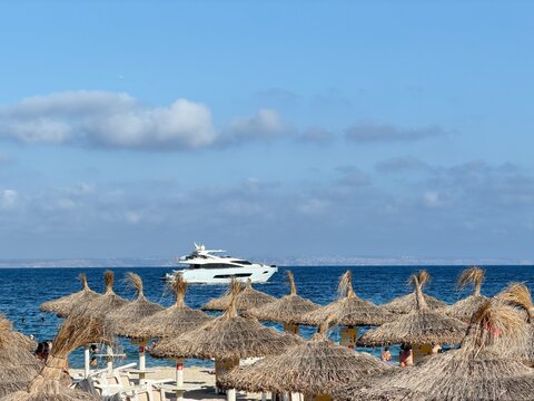 Luxury yacht sailing on the balearic sea off calvia beach, spain, offering an iconic view over numerous straw umbrellas and sun loungers for summer holidays