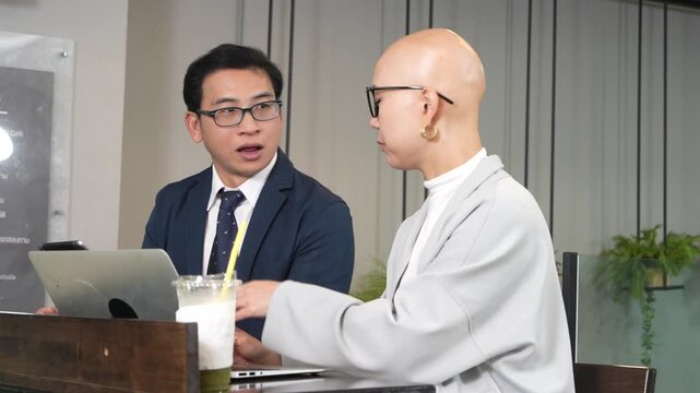 A smart-looking Korean female employee wearing glasses sits with an Asian male colleague in a coffee shop, working on her laptop, reading emails, and attending a meeting.
