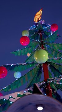 Festive christmas tree with a star topper, illuminated by vibrant, colorful glowing lights and shiny baubles against the dark evening sky, creating a magical holiday atmosphere
