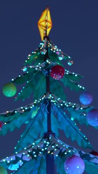 Colorful illuminated artificial christmas tree decorated with a bright star topper, baubles, and festive string lights shining against a deep blue evening sky, creating a magical holiday mood