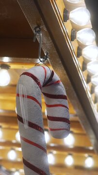 Close up of a glittery red and white candy cane ornament hanging at a festive christmas market, warm incandescent lights glowing in the background with soft bokeh effects