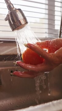 Vertical video. Woman Rinses Fresh Red Tomato beneath Spraying Kitchen Faucet in Slow Motion, Food Safety and Healthy Meal Preparation