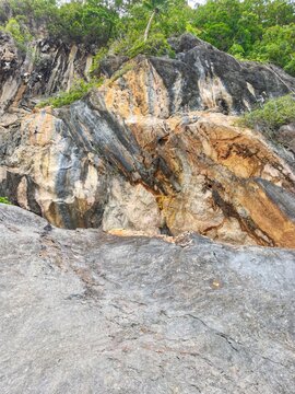 Dramatic geological mountain cliff face with colorful mineral strata and lush green trees