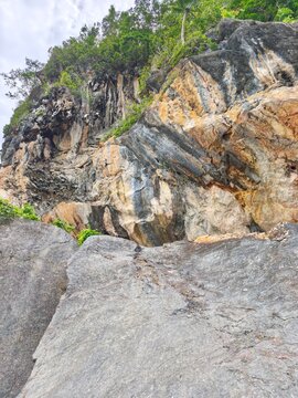 Massive colorful geological cliff face with steep rocky slope and green forest trees against sky