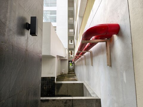 Industrial red water pipes installed on exterior wall of modern building in narrow corridor perspective