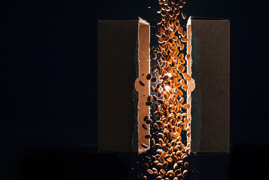 Roasted coffee beans spilling from a torn package on black background